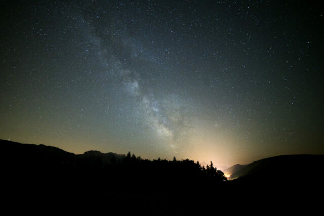 Depuis le col de la Croix Perrin, en été, la Voie lactée est particulièrement spectaculaire. En regardant vers la constellation du Sagittaire, nous tournons notre regard vers le centre de notre galaxie, situé à environ 27 000 années-lumière de la Terre. Là se trouve Sagittarius A*, un trou noir supermassif d’environ quatre millions de masses solaires. Cette région est la plus lumineuse et la plus épaisse de la Voie lactée, car elle contient une très forte concentration d’étoiles, de nuages de gaz et de poussières interstellaires.